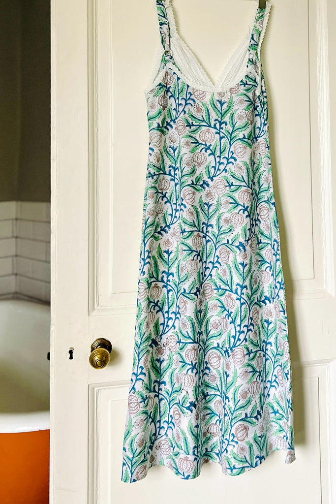 Back view of strappy V neck nightdress in green and blue floral print on white ground with white lace trim hanging on bathroom door