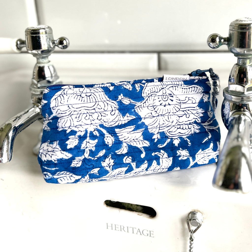 Small make up bag in blue and white floral print with beaded zip pull sitting on a white wash basin