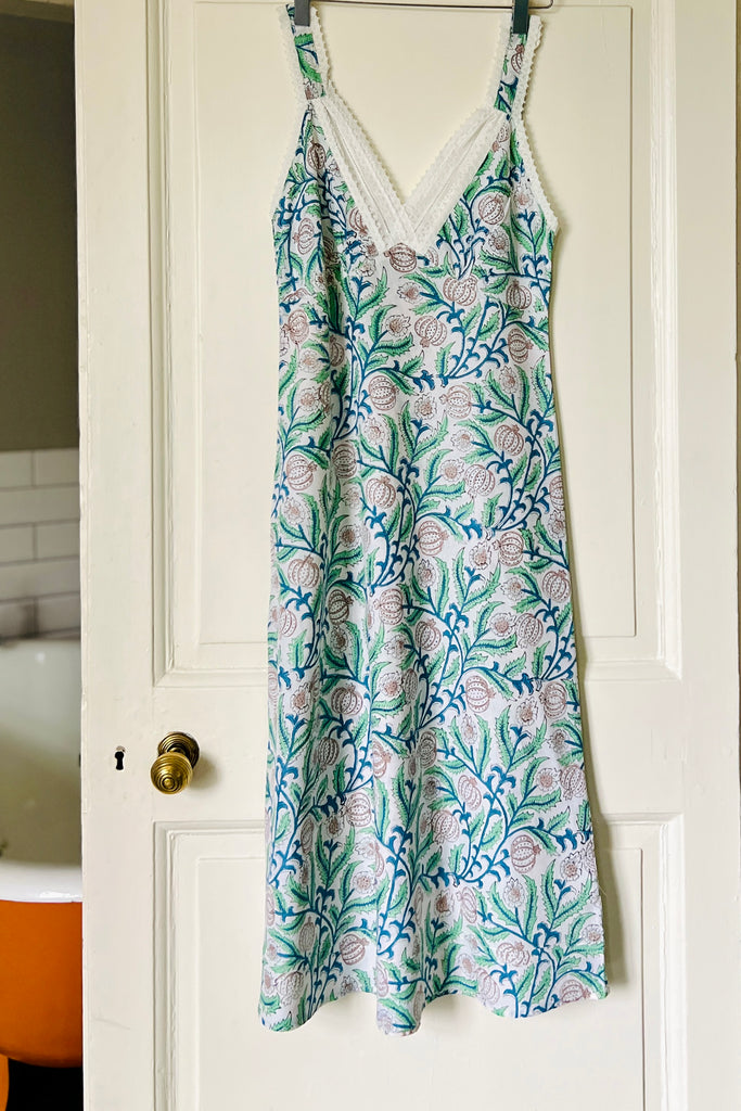 Strappy V neck nightdress in green and blue floral print on white ground with white lace trim hanging on bathroom door