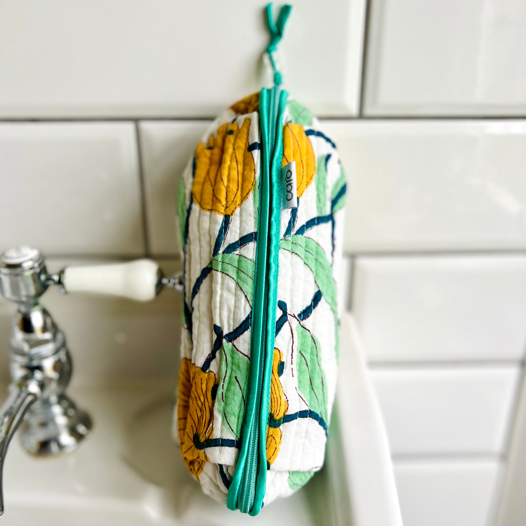 large scale yellow, green and white floral print long quilted make up bag leaning on wash basin