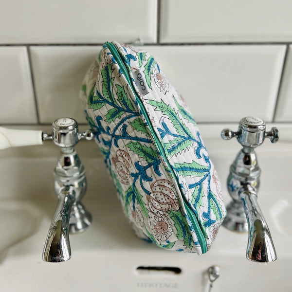 Arts & Crafts inspired floral print long quilted cotton print make up bag with extra long zip sitting on wash basin. 