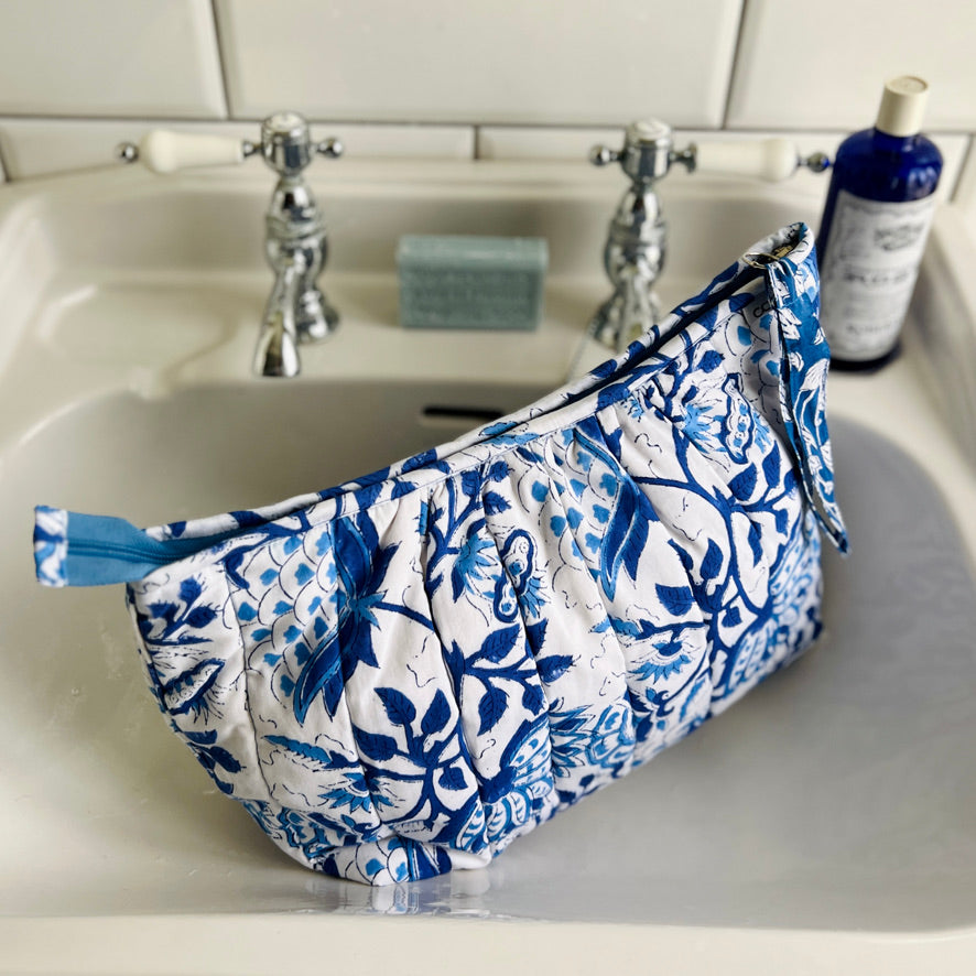 Large Caro London blue floral on white ground quilted cotton washbag sitting in a wash basin