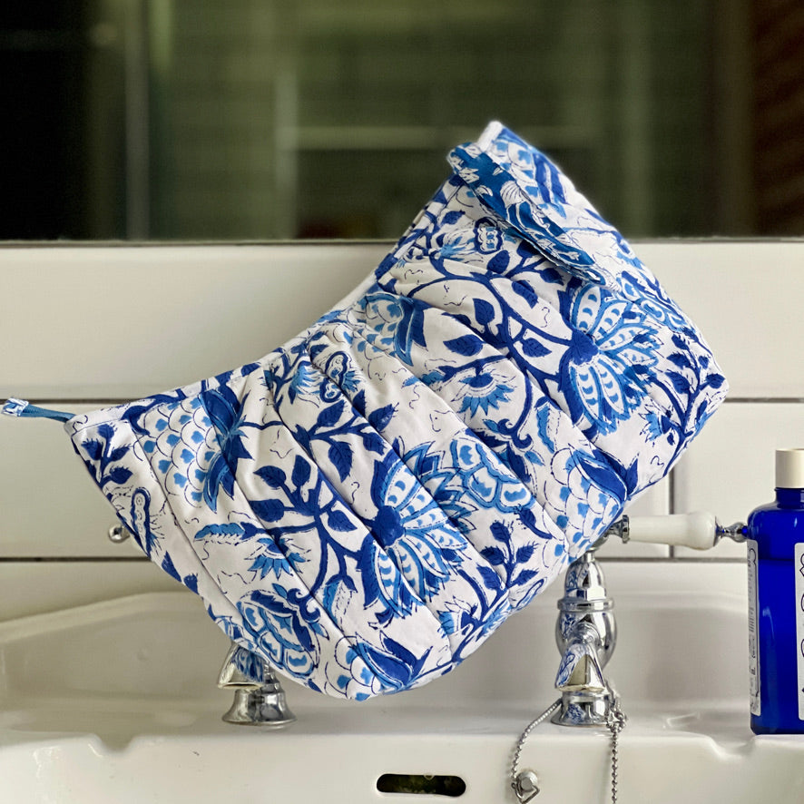 Large Caro London blue floral on white ground quilted cotton washbag sitting on wash basin