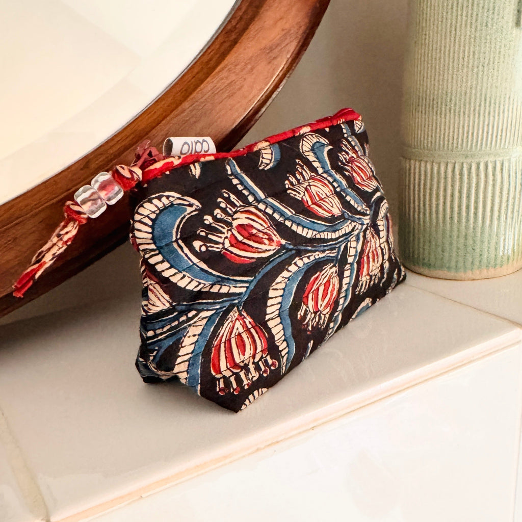 close up view of our best selling mini make up bag made from quilted cotton hand block print in black, cream, blue and red showing beaded zip pull, contrast red trim and brand label