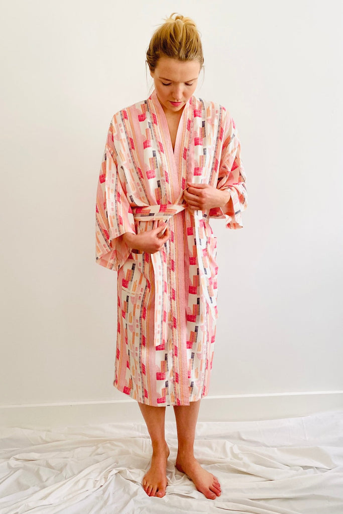  woman tieing a belt of a knee length kimono in geometric print red,pink and white